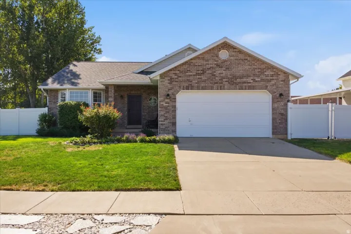 Brick facade residence featuring an attached two-car garage, a concrete driveway, and a white vinyl fence