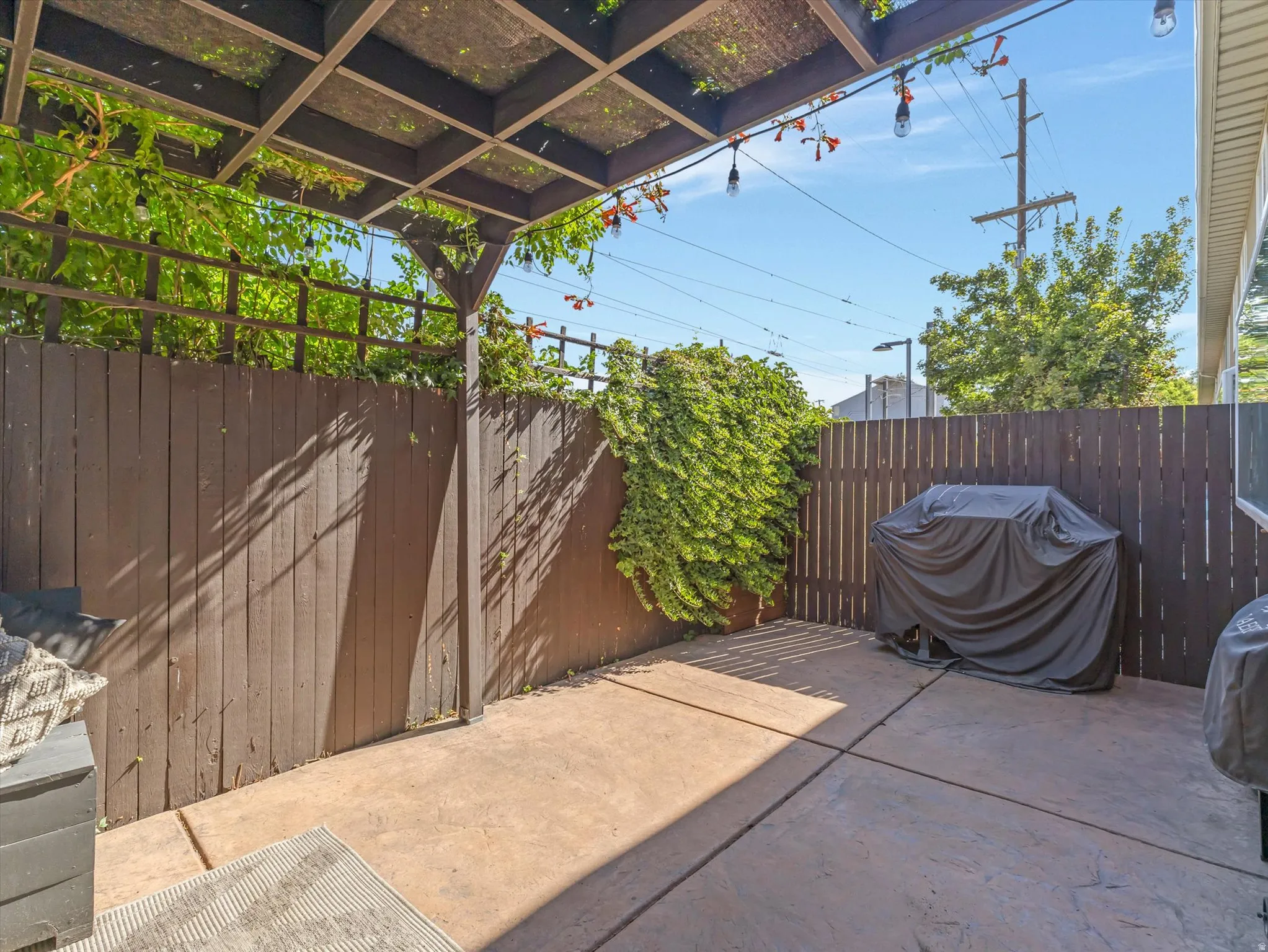 Private patio space featuring a concrete surface, a slatted privacy fence, and an overhead pergola with string lighting
