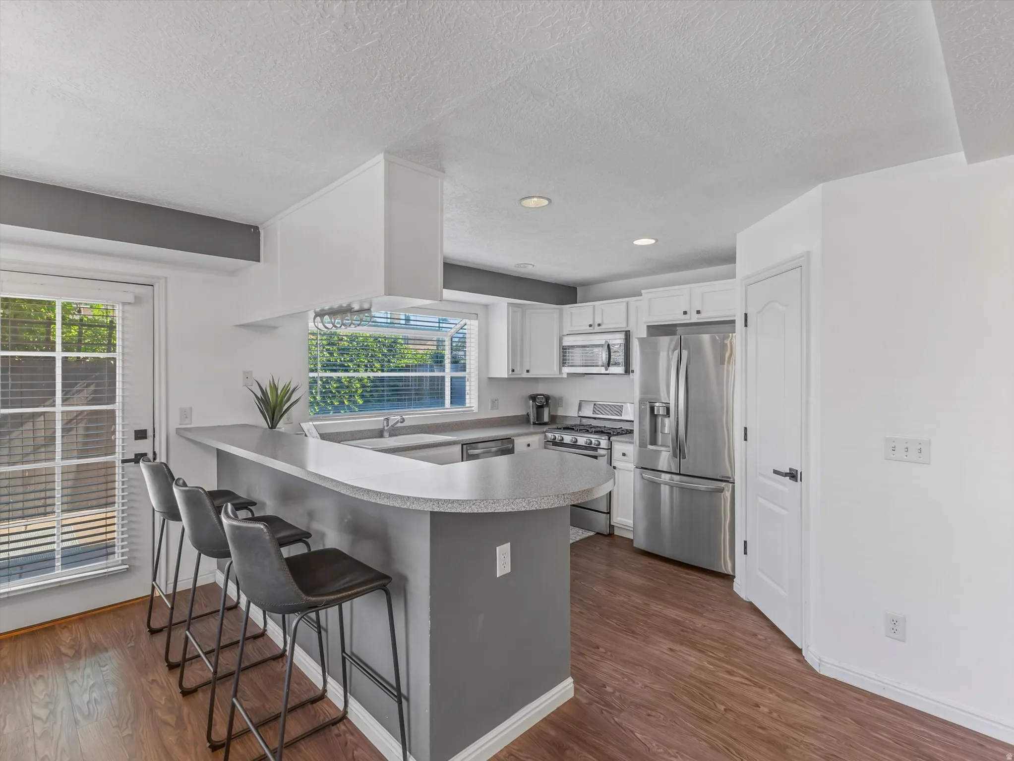 Kitchen featuring an eat-at peninsula with a light-toned countertop, white cabinetry, stainless steel appliances, wood-finish flooring, and a glass-paned exterior door