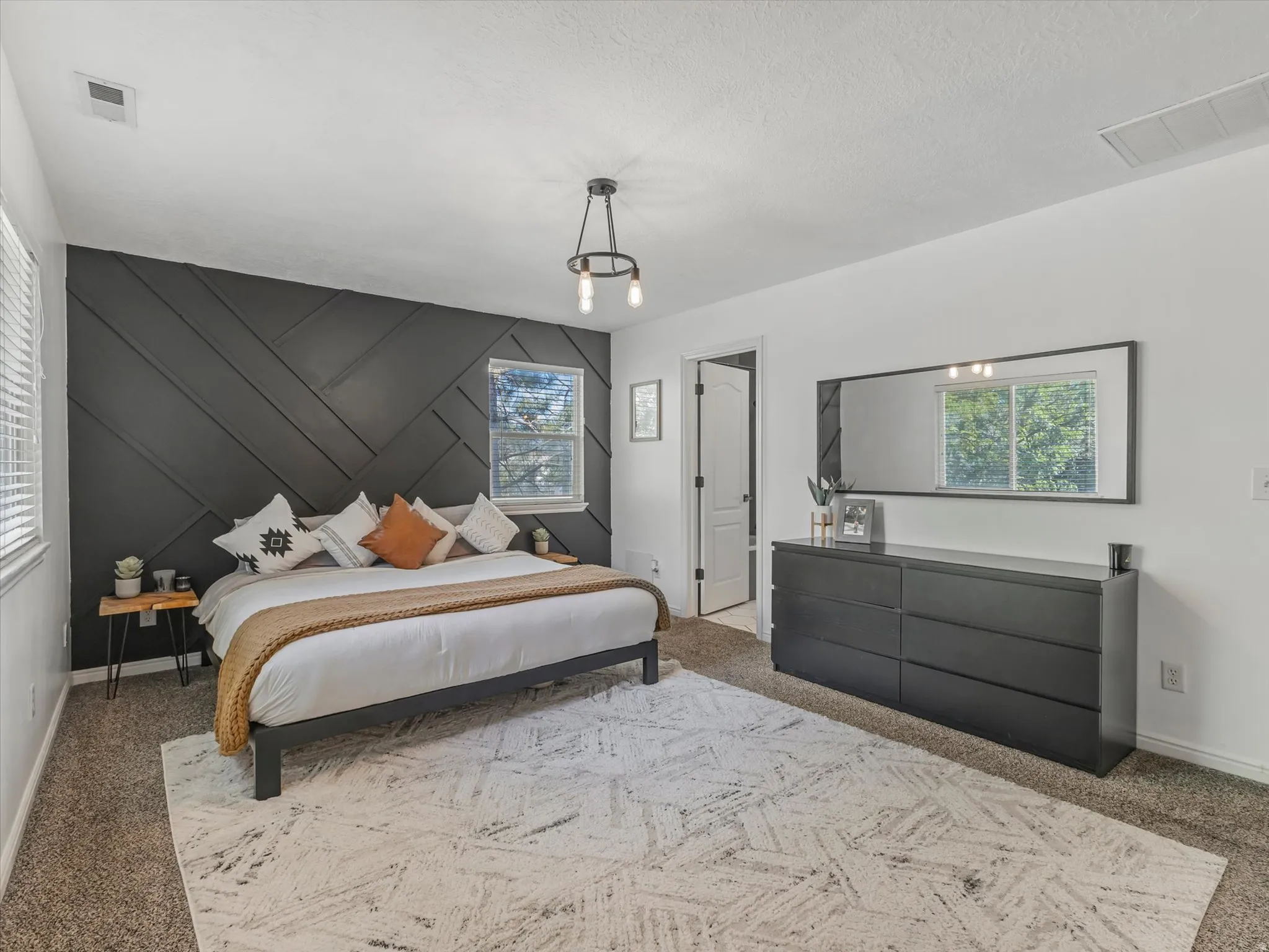 Accent wall with geometric paneling, two windows with blinds, ceiling-mounted light fixture, and carpet flooring