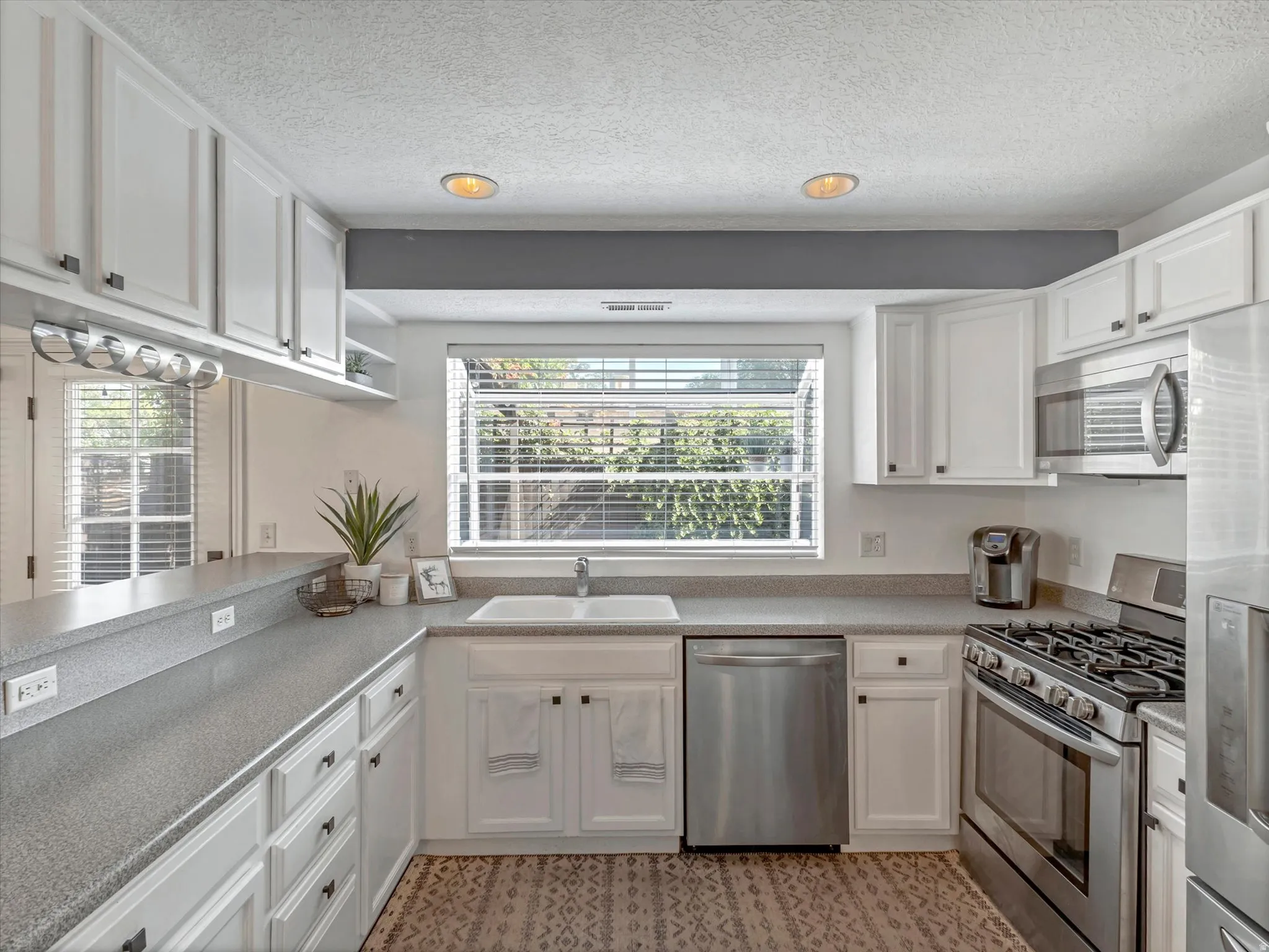 Kitchen featuring white cabinetry, gray speckled countertops, stainless steel appliances, a double basin sink, and recessed lighting