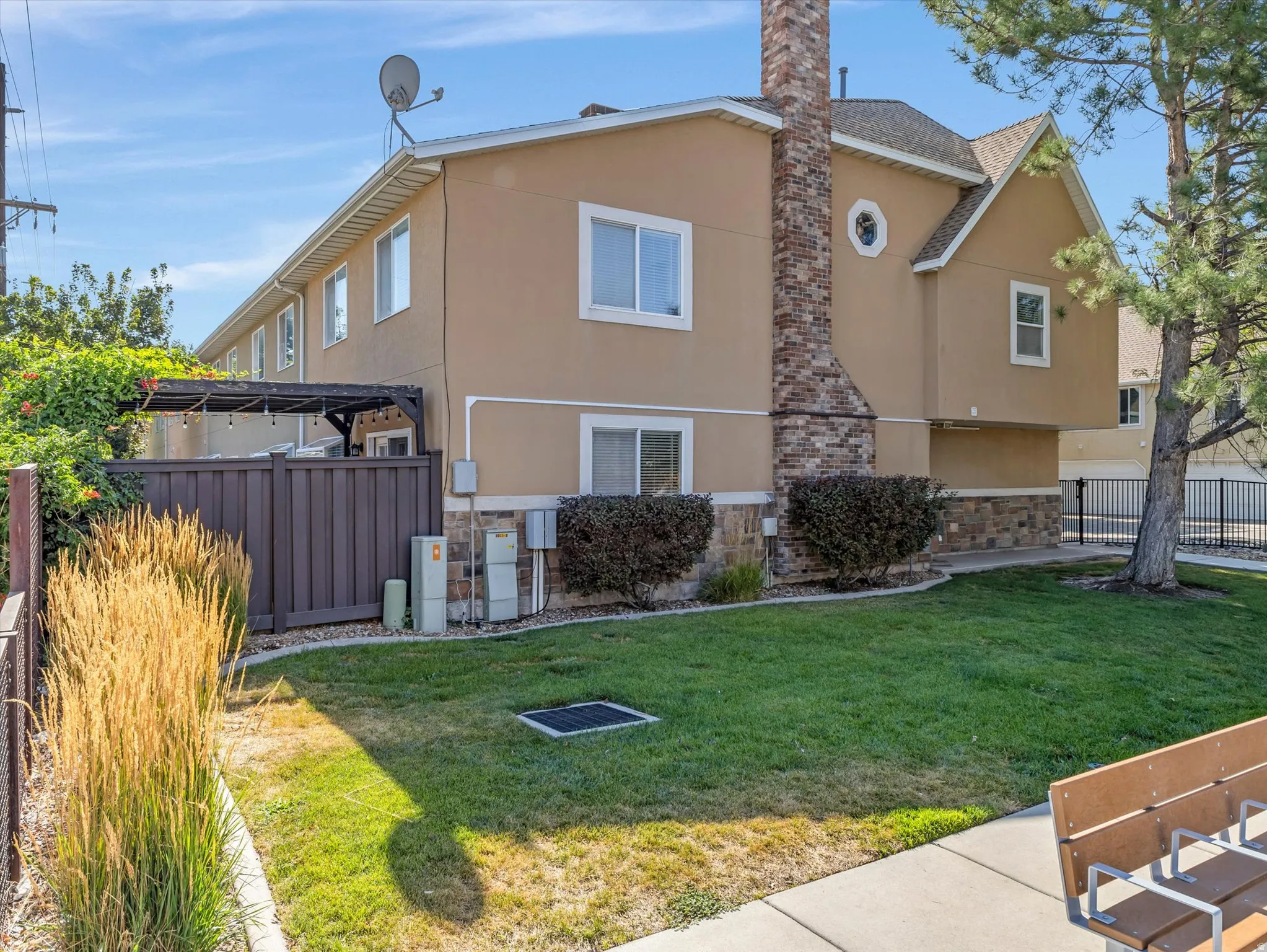 Stucco exterior with a stone veneer foundation, a side patio featuring a wood pergola, privacy fencing, and a manicured lawn