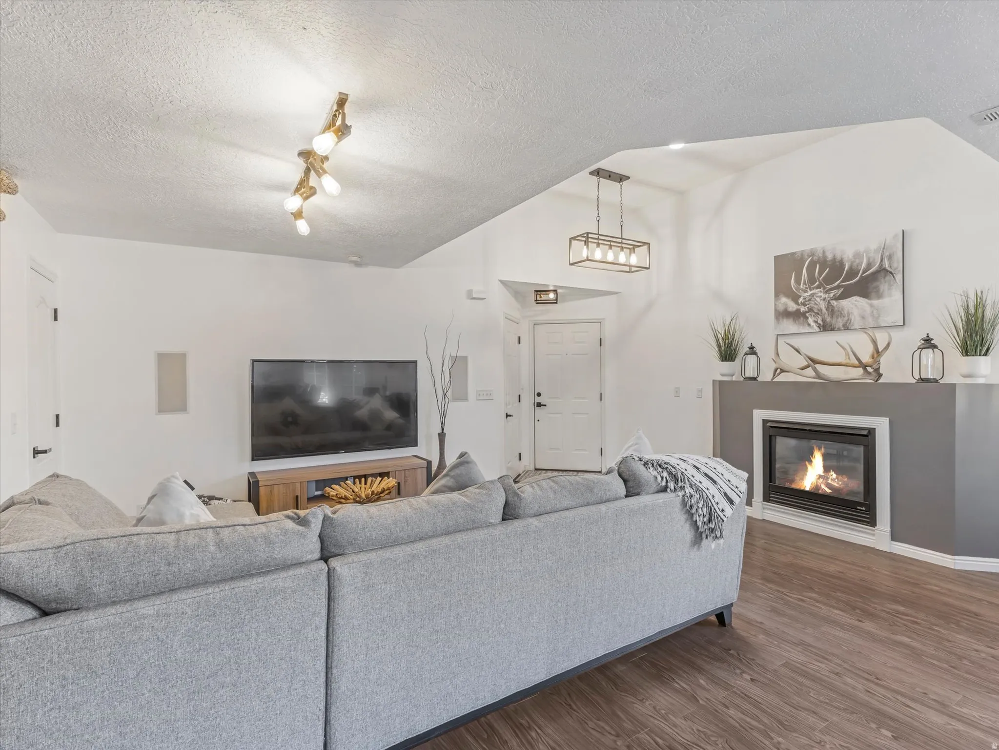 Spacious living area featuring vaulted ceilings, wood-finish flooring, a contemporary fireplace with a wide mantel, and a stylish rectangular chandelier