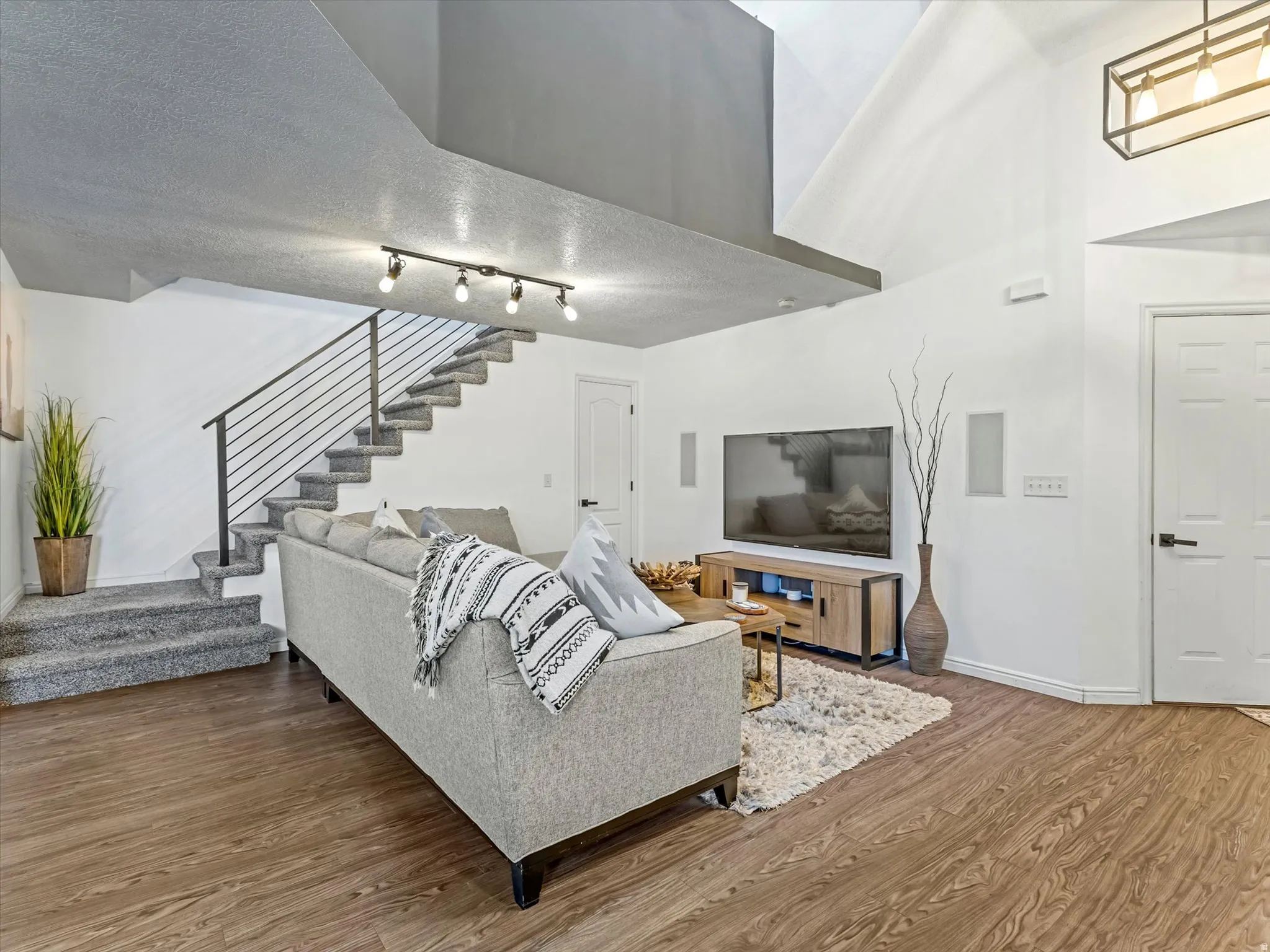 Living area featuring wood-finish flooring, a carpeted staircase with a modern metal railing, and vaulted ceilings