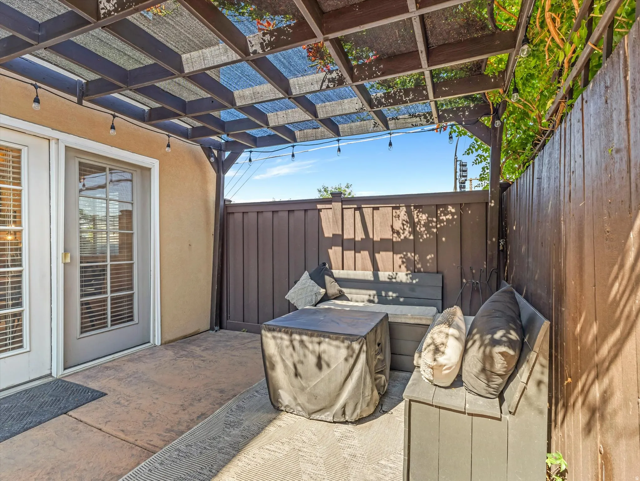 Private outdoor patio featuring a wooden pergola with shading, stamped concrete flooring, and a privacy fence