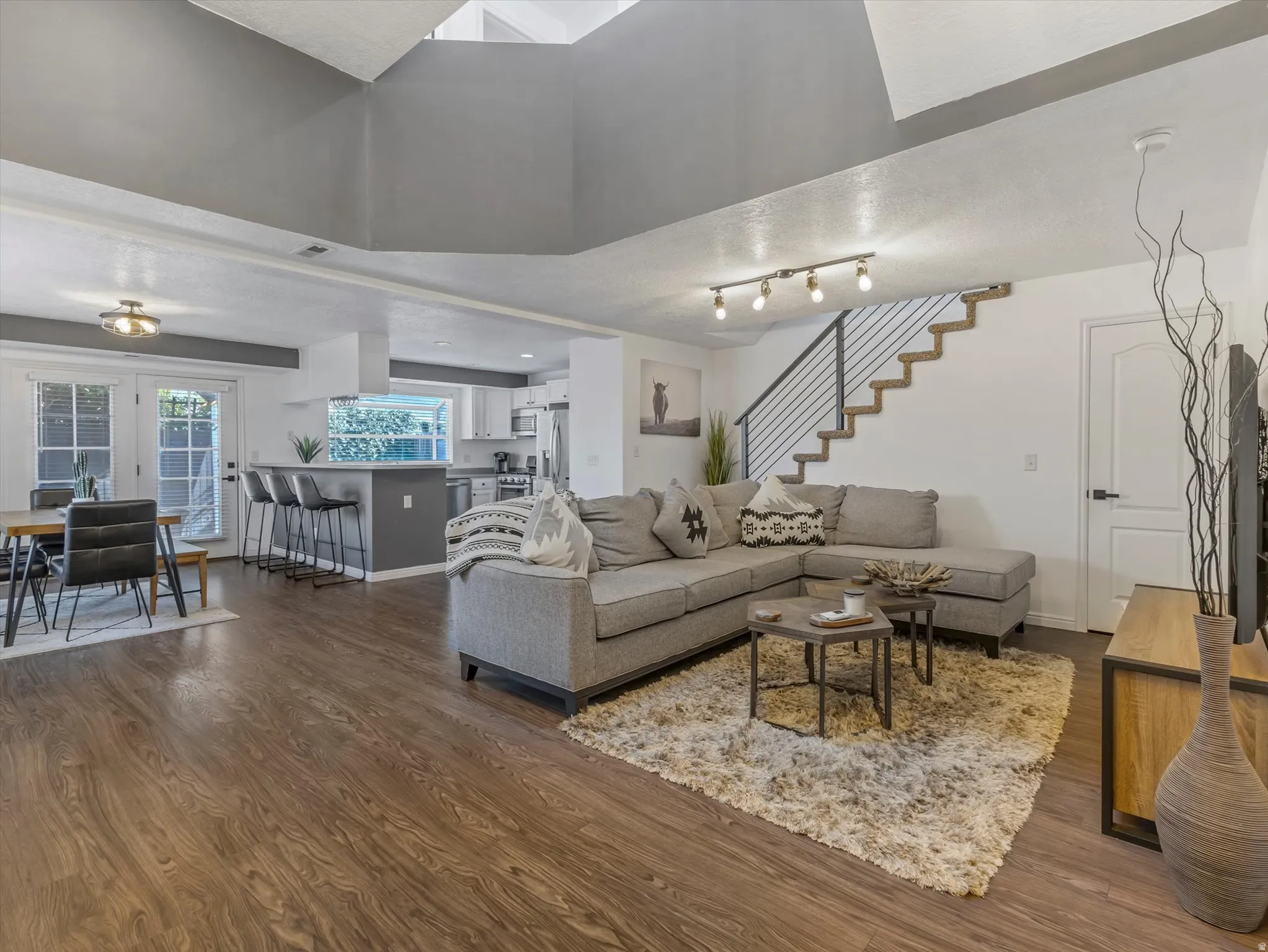 Open-concept living space featuring wood-finish flooring, a contemporary staircase with metal railings, and a kitchen with an island and pendant lighting