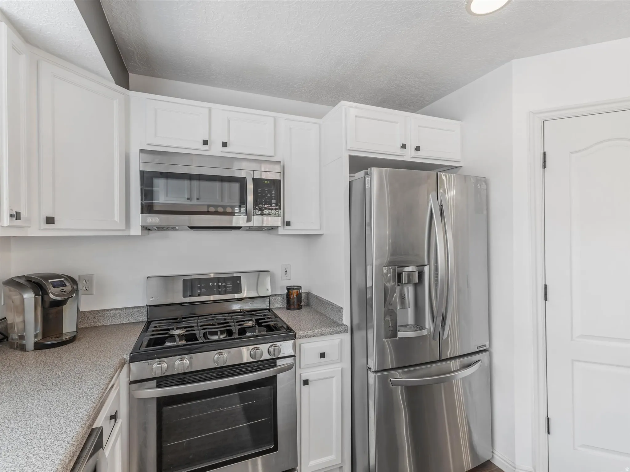 Kitchen featuring white cabinetry, stainless steel appliances, speckled countertops, and a white paneled door
