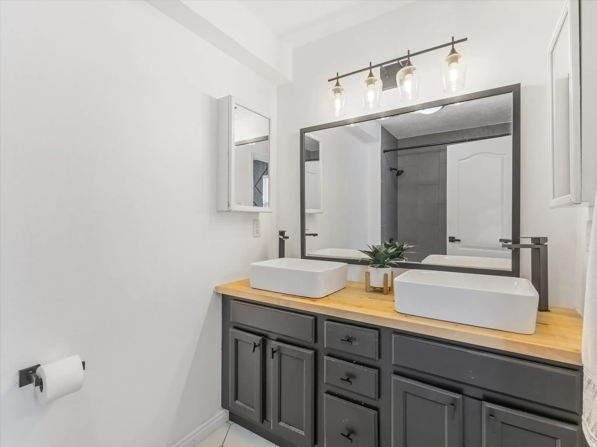 Double vanity featuring dark gray cabinetry, natural wood-finish countertop, and two rectangular vessel sinks