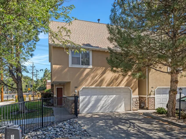 Two-story stucco exterior featuring an attached two-car garage, stone accents, and a fenced front yard with mature trees