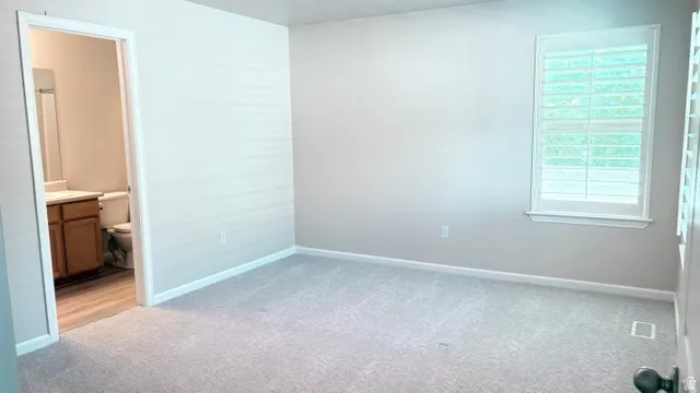 Spacious room featuring light gray carpeting, a window with plantation shutters, and light gray wall paint