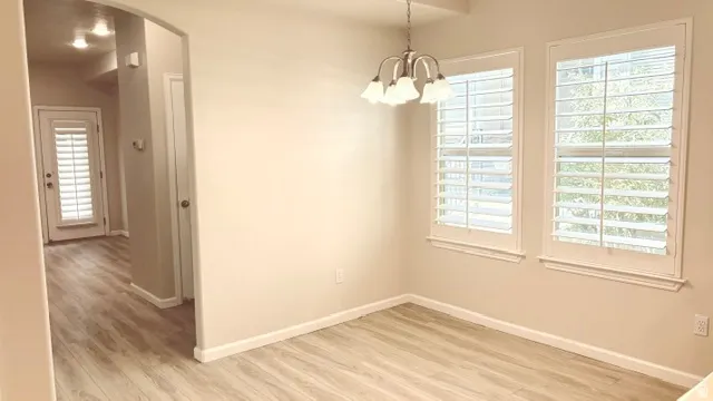 Dining area featuring two windows with white plantation shutters, a chandelier with frosted glass shades, light wood-finish flooring, and a neutral paint palette