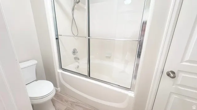 Full bathroom featuring a shower-over-tub combination with sliding glass doors, white toilet, and wood-finish flooring