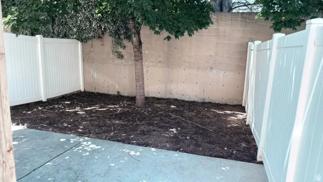 Enclosed outdoor space featuring a mature tree, concrete patio, and white privacy fencing