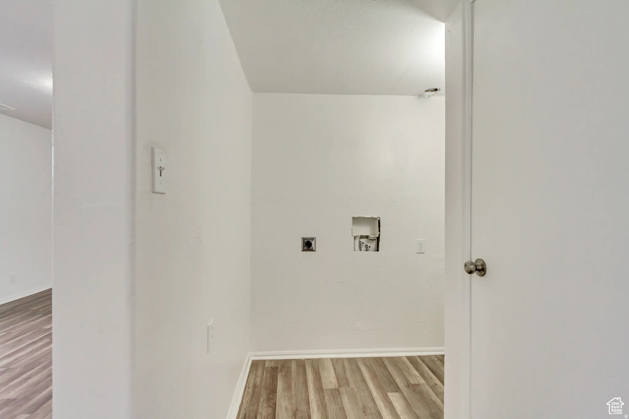 Dedicated laundry area featuring wood-finish flooring, white walls, and essential utility hookups