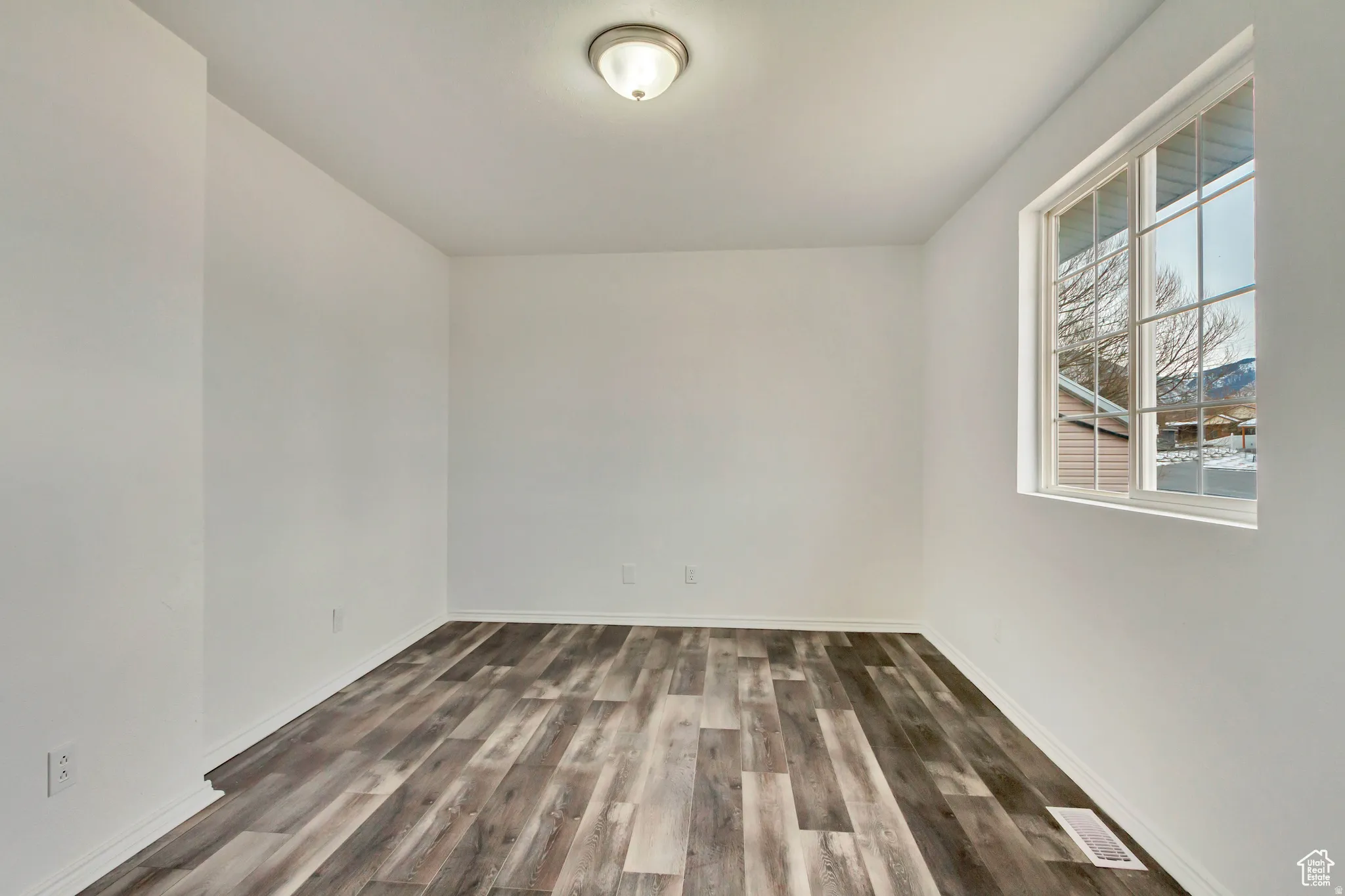Room featuring neutral white walls, wood-finish flooring, and a multi-pane window