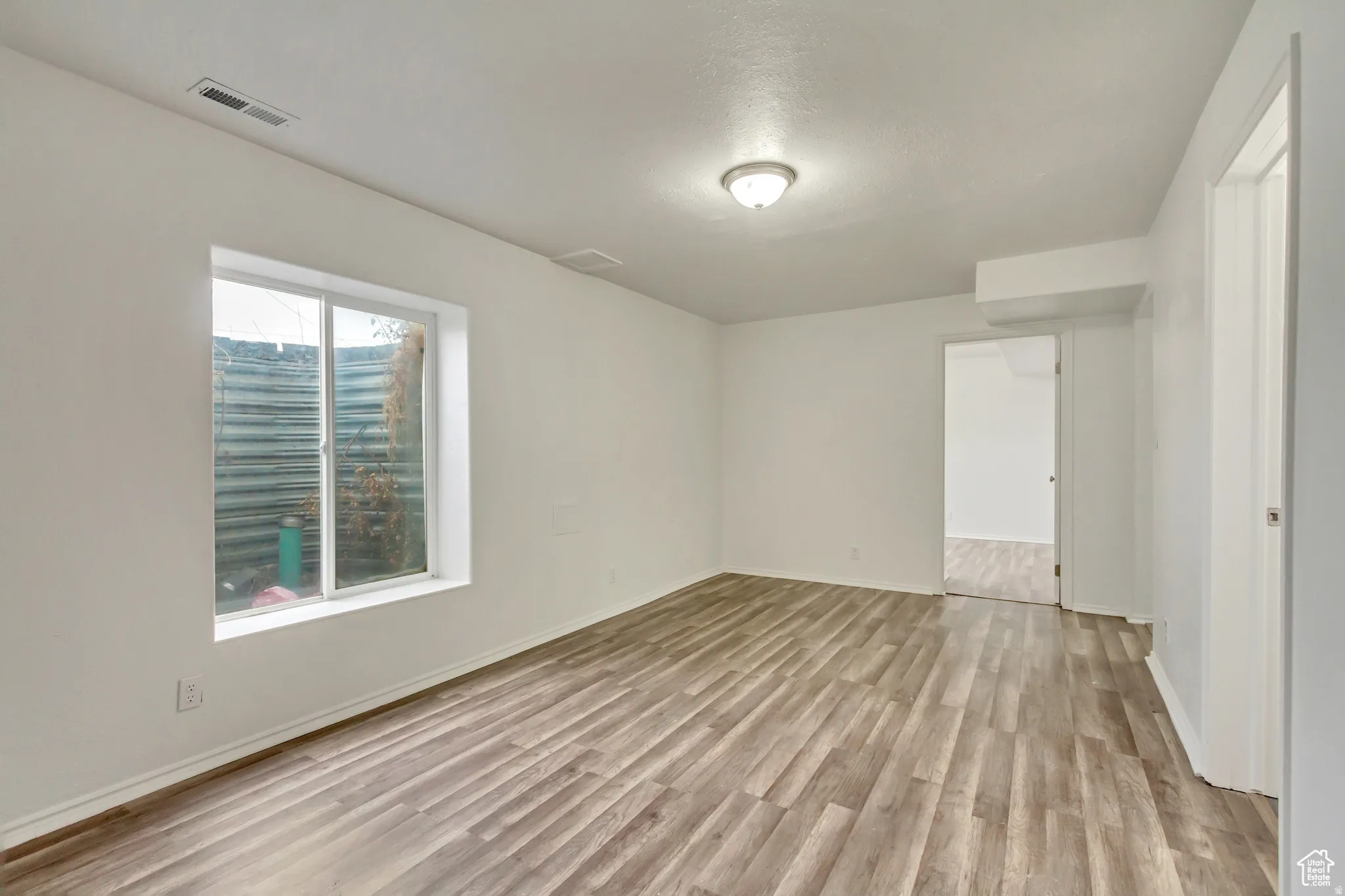 Spacious room featuring wood-finish flooring, white walls, and a ceiling-mounted light fixture
