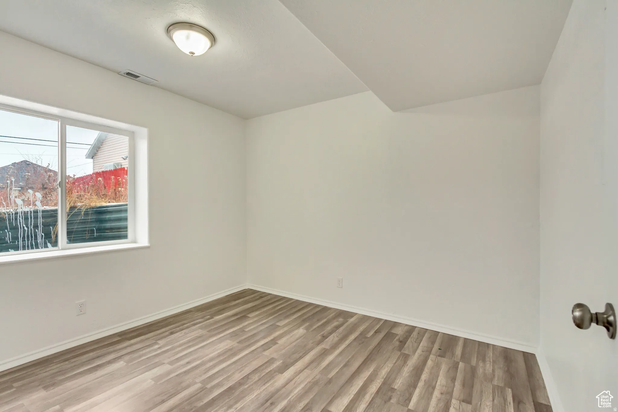 Room featuring wood-finish flooring, white baseboards, a single window, and a flush mount ceiling light