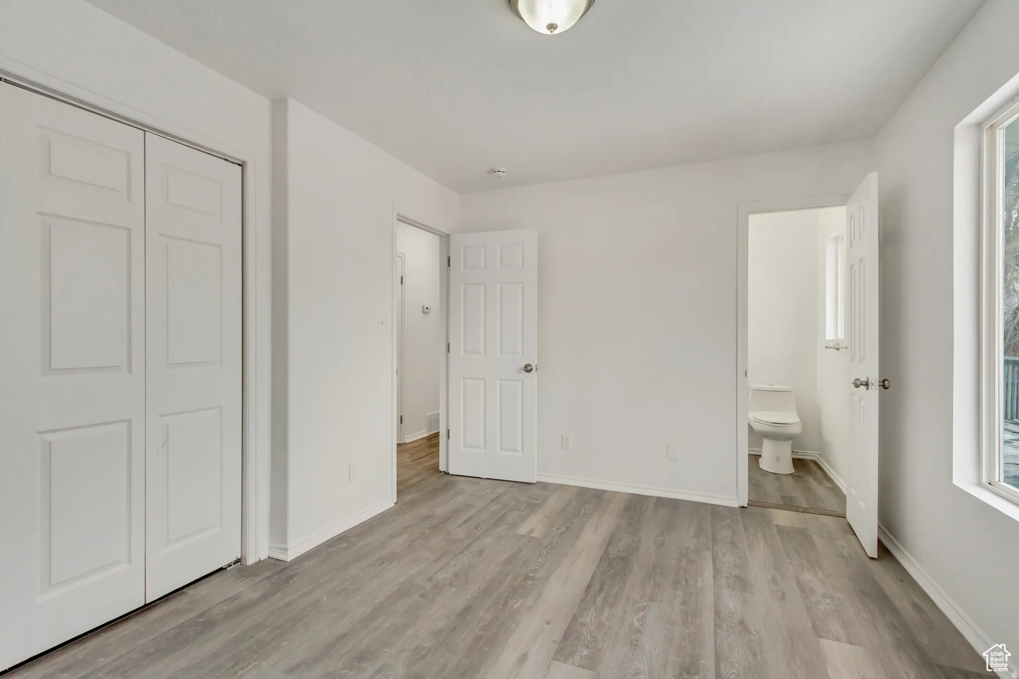 Spacious room featuring light-toned wood-finish flooring, white walls, and a ceiling-mounted light fixture