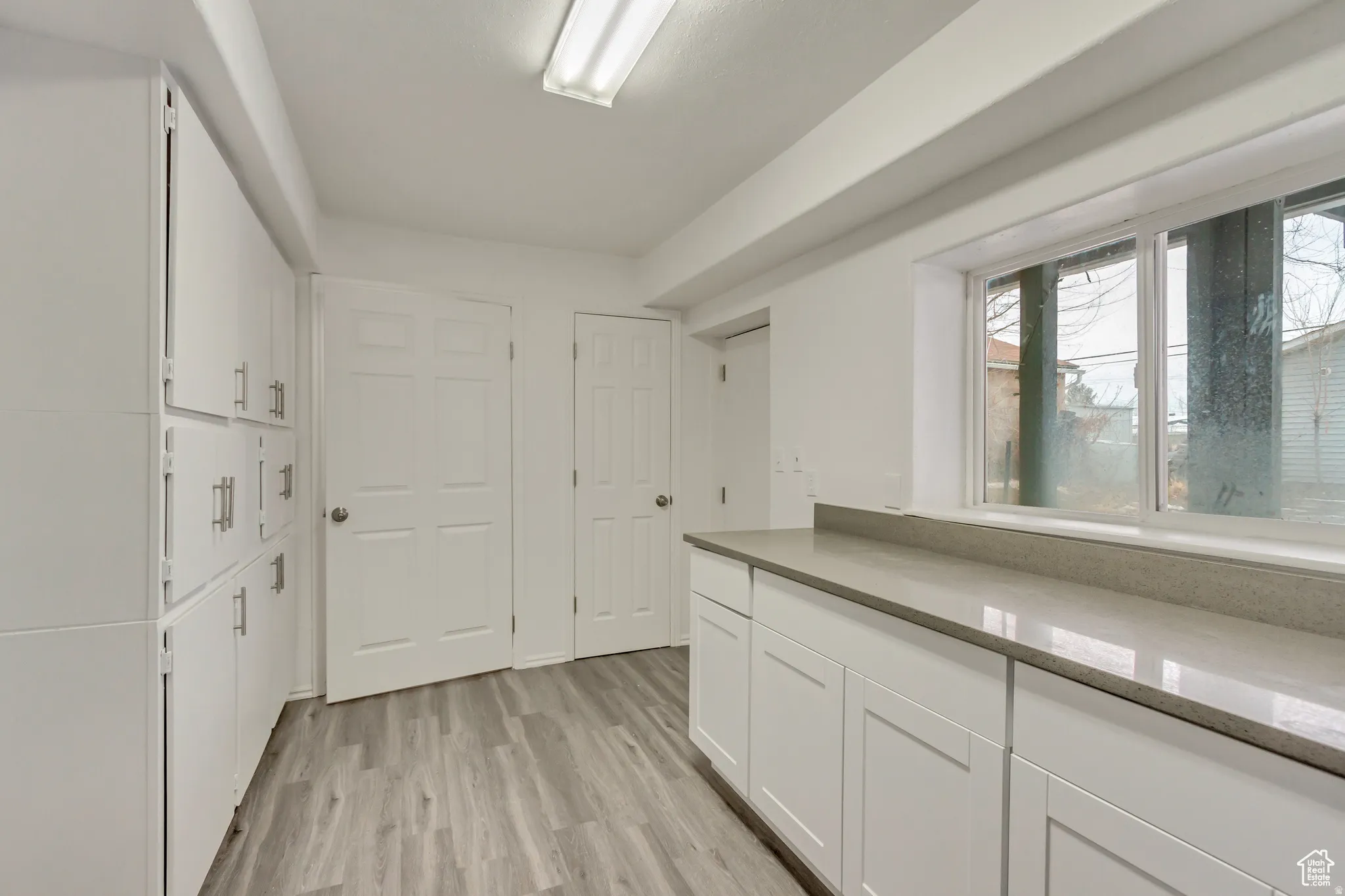 Utility room featuring extensive white cabinetry with silver hardware, light gray countertop space, a window, and wood-finish flooring