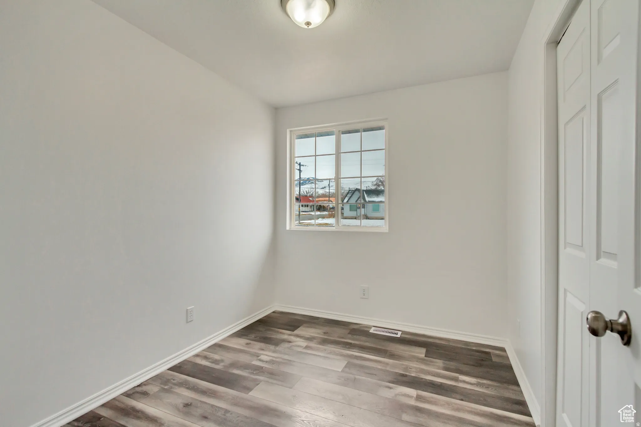 Room featuring wood-finish flooring, white walls, and a window with grid panes