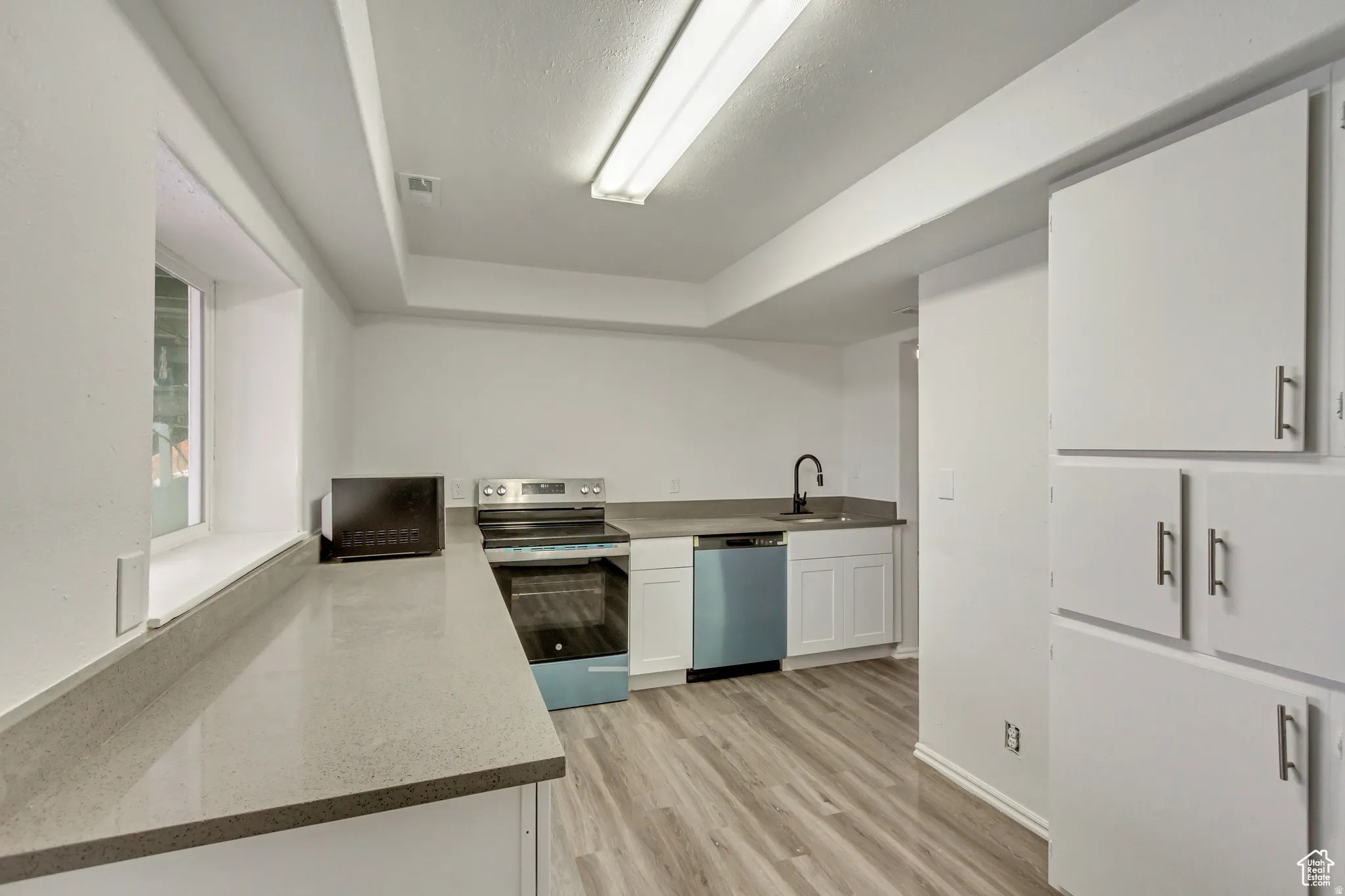 Kitchen featuring light wood-finish flooring, white cabinetry with contemporary hardware, light-toned countertops, a stainless steel range, and a black faucet