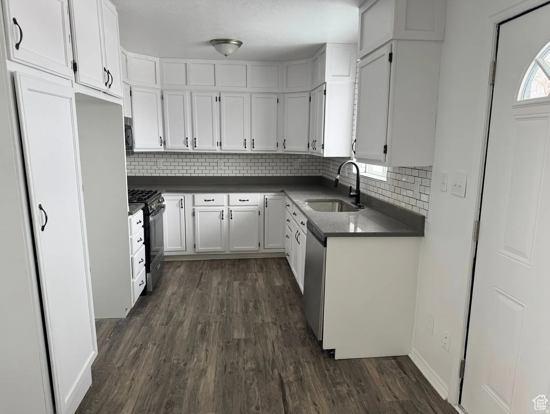 Updated Kitchen with White Cabinetry, Subway Tile Backsplash, and Dark Wood-Finish FlooringThis galley-style kitchen features crisp white cabinetry with brushed nickel hardware, stainless steel appliances including a gas range and dishwasher, and a subw