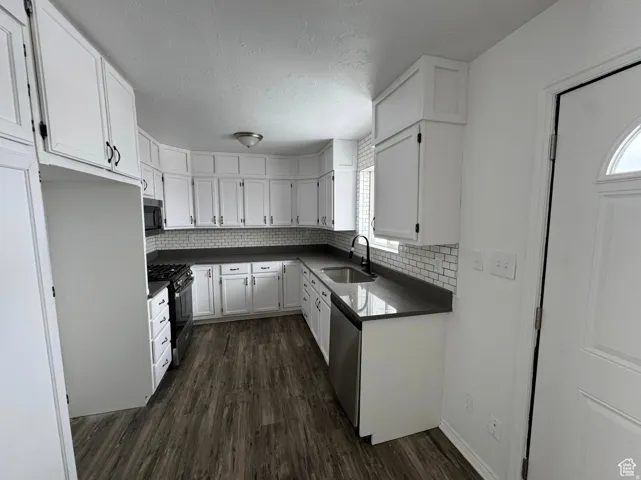 Modern kitchen featuring crisp white cabinetry with brushed nickel hardware, black countertops with subway tile backsplash, stainless steel appliances, and wood-finish flooring throughout