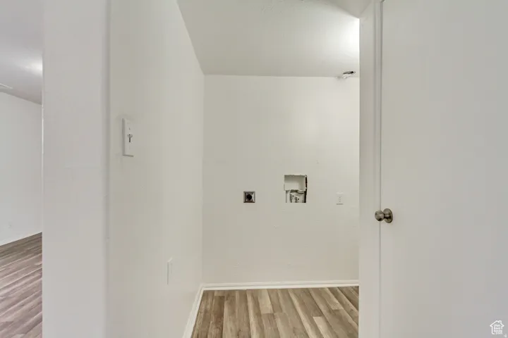 Dedicated laundry area featuring wood-finish flooring, white walls, and essential utility hookups