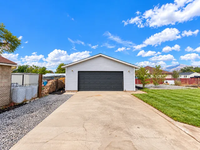 Detached garage with horizontal siding, a dark paneled garage door, concrete driveway, and gravel landscaping
