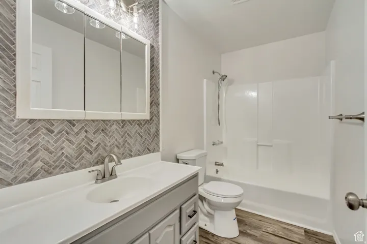 Bathroom featuring a herringbone tile accent wall, white vanity with integrated sink, brushed nickel faucet, three-door mirrored medicine cabinet, and wood-finish flooring