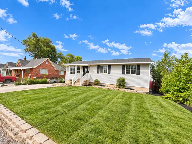 Siding exterior with dark shutters, front entry porch, and a large lawn with a retaining wall