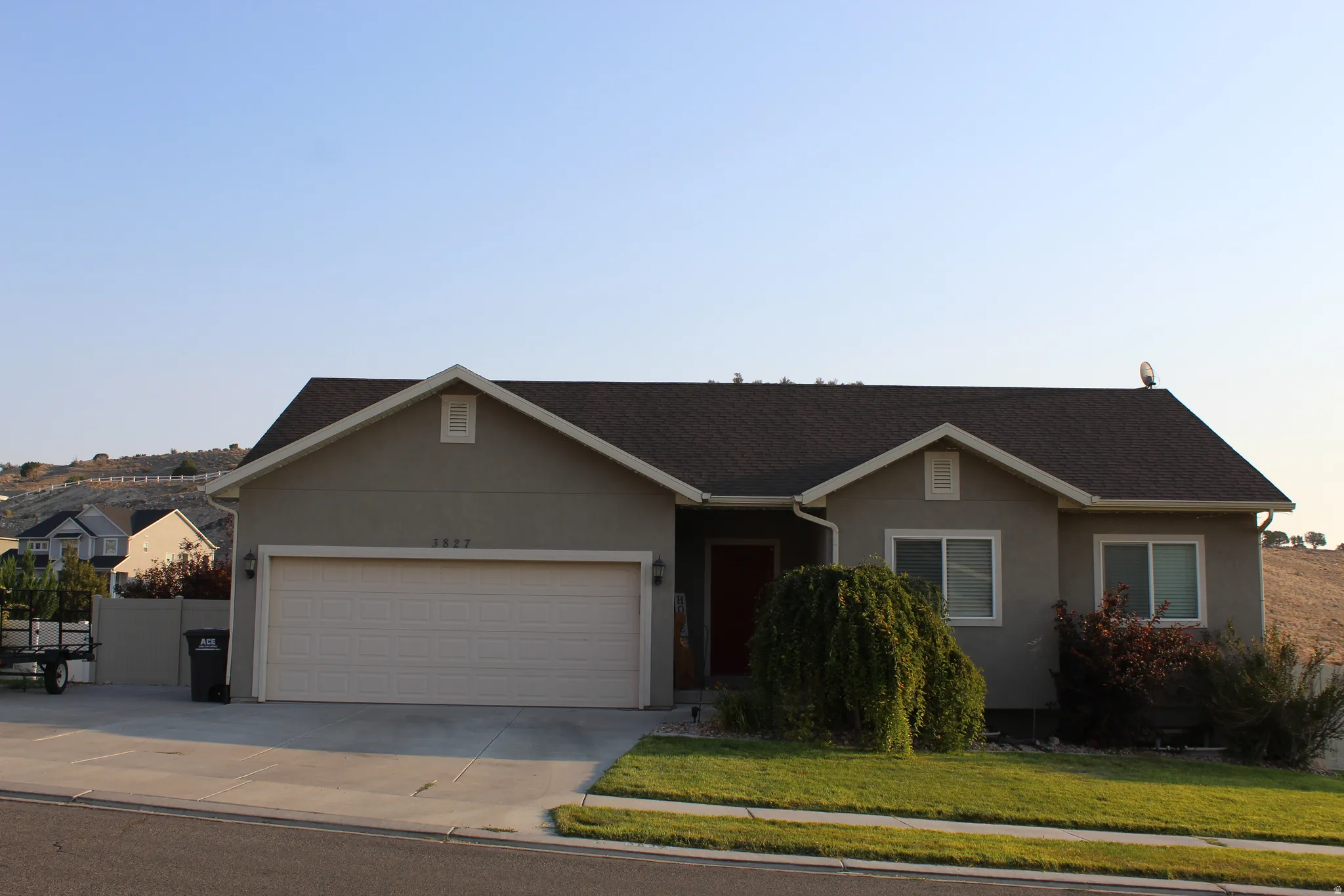 Ranch-style residence featuring a taupe stucco exterior, a dark shingle roof, and a two-car garage with a light-colored door