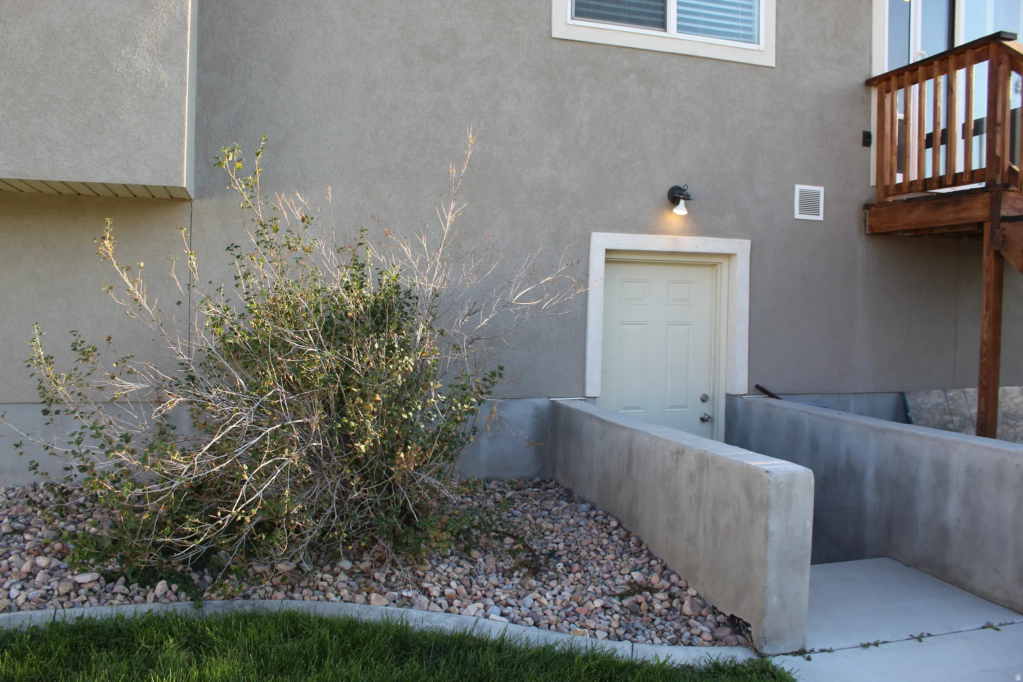 Concrete exterior with a stucco finish, featuring a white paneled door with trim, exterior wall sconce, and a concrete-lined egress