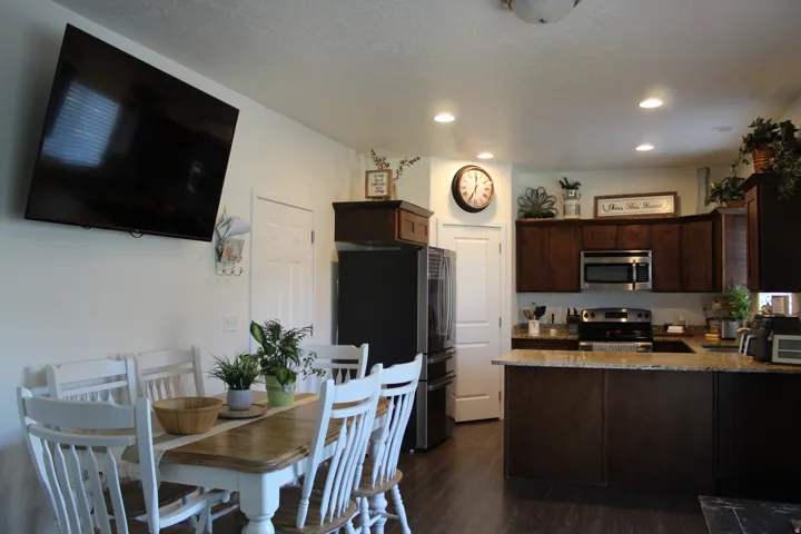 Recessed lighting illuminates the kitchen, featuring stainless steel appliances, dark wood cabinetry, and a light-toned countertop