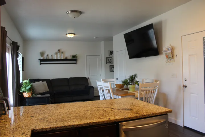 Open-concept living space featuring a granite-style countertop, stainless steel dishwasher, and wood-finish flooring