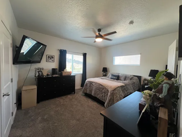 Carpeted flooring, vaulted ceiling, ceiling fan with integrated lighting, and multiple windows with blinds