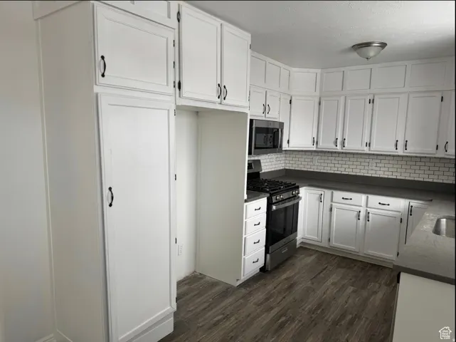 Modern kitchen featuring extensive white cabinetry with matte black hardware, dark countertops, white subway tile backsplash, and wood-finish flooring