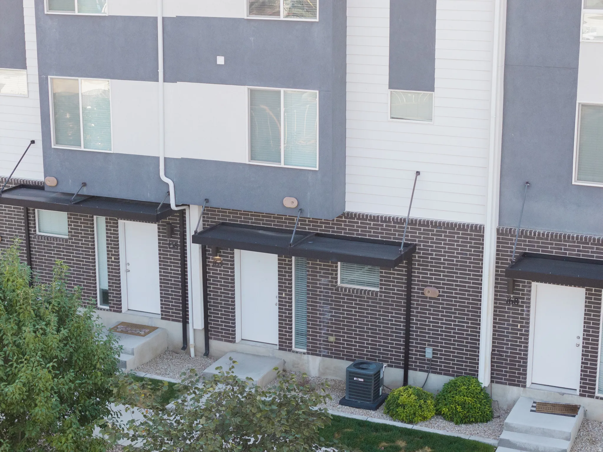 Contemporary townhome exterior featuring a combination of gray stucco, white siding, and brick accents