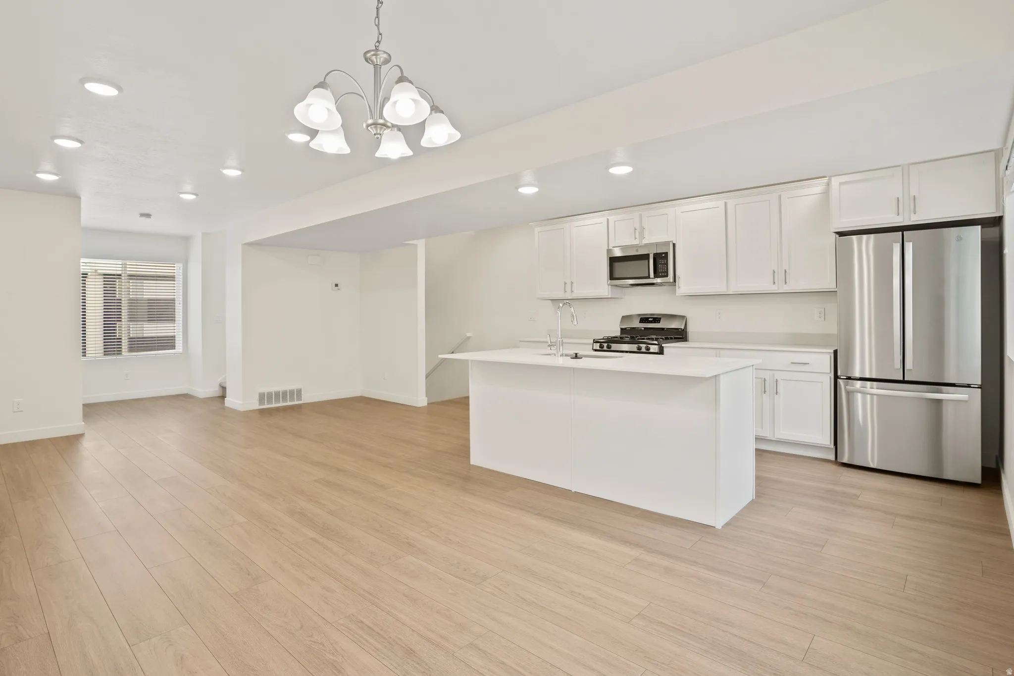 Open-concept kitchen and living area featuring wood-finish flooring, recessed lighting, and a chandelier