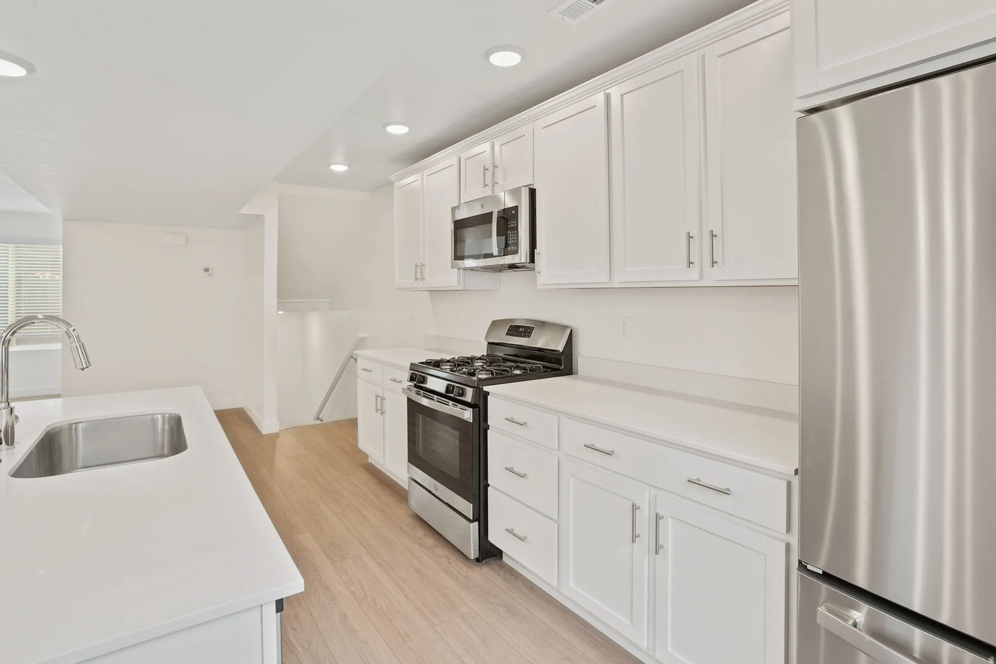Modern kitchen featuring white shaker cabinetry, stainless steel appliances, light wood-finish flooring, recessed lighting, and white countertops