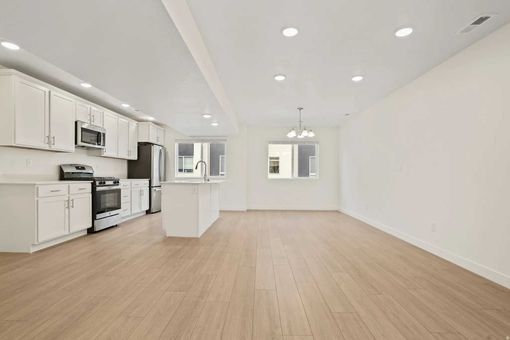 Open-concept living space featuring wood-finish flooring, recessed lighting, and a kitchen with white cabinetry