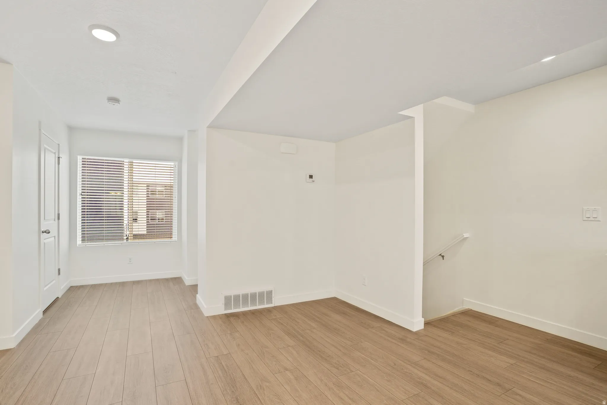 Spacious interior featuring wood-finish flooring, recessed lighting, and a large window with horizontal blinds