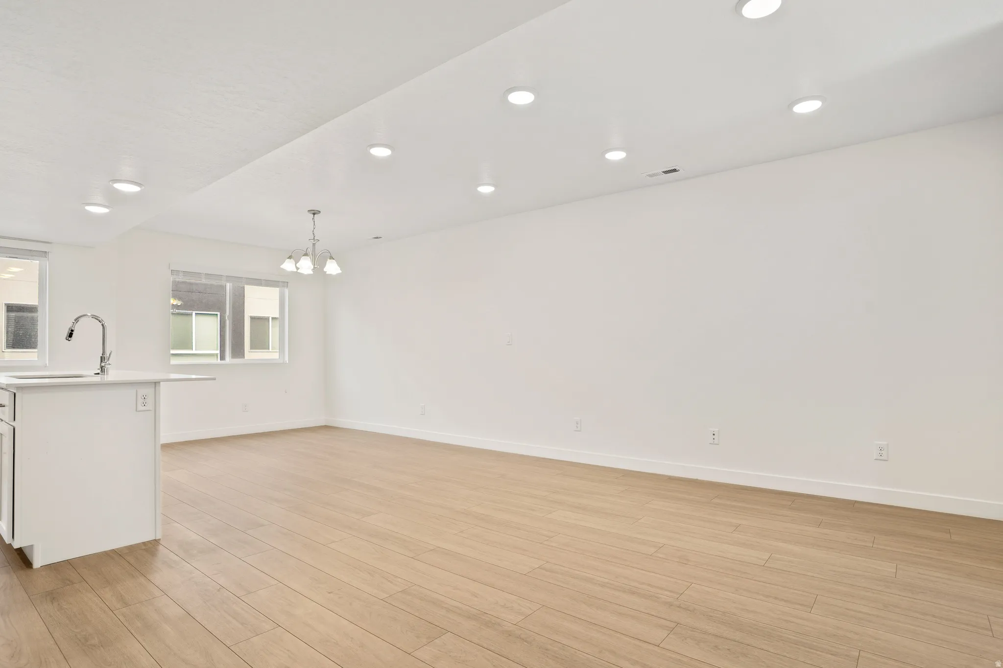 Open-concept living area featuring light wood-finish flooring, recessed ceiling lighting, and a modern chandelier