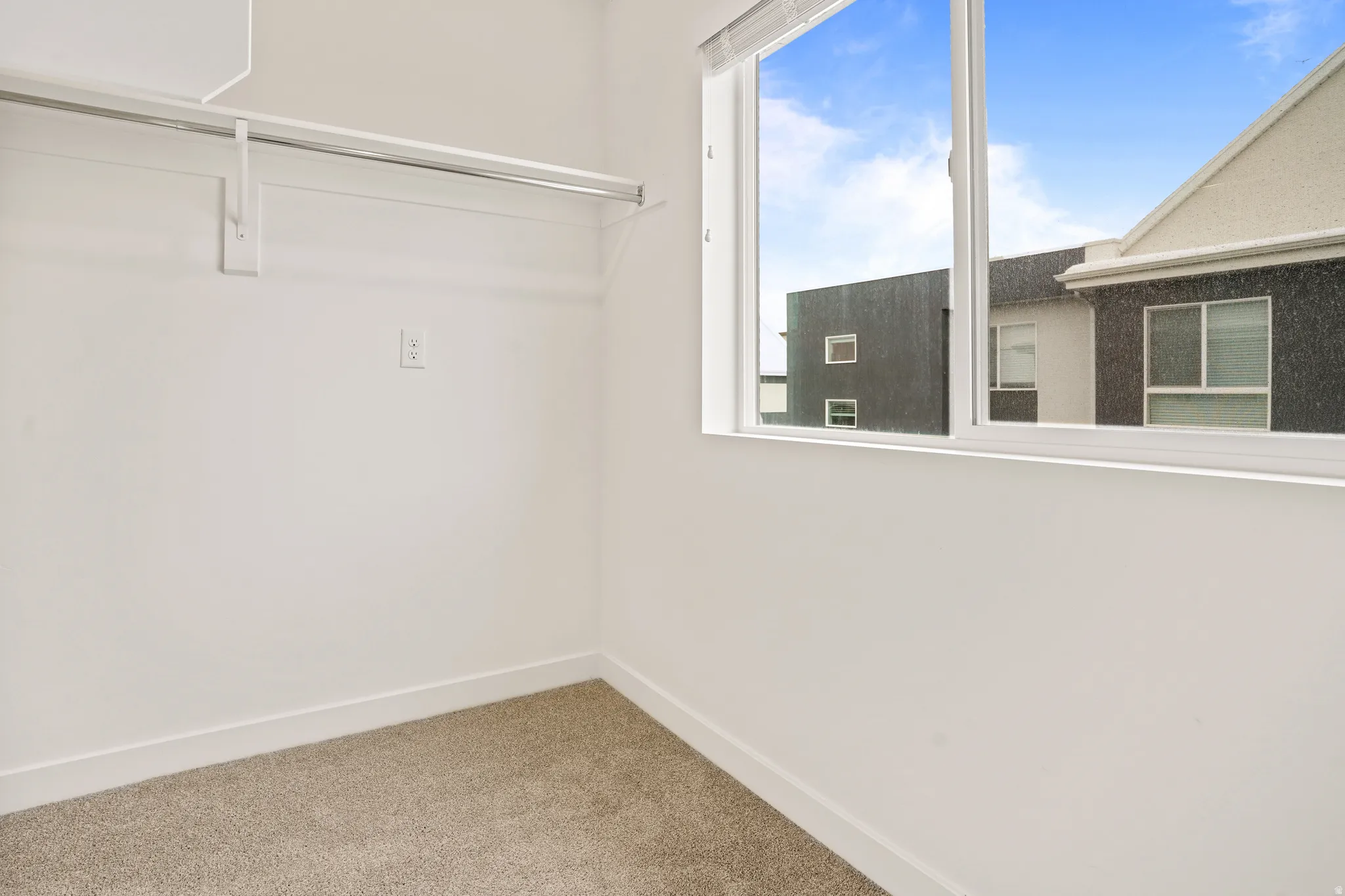 Room featuring light tan carpeting, a single window with white framing, and a white clothes rod with shelf