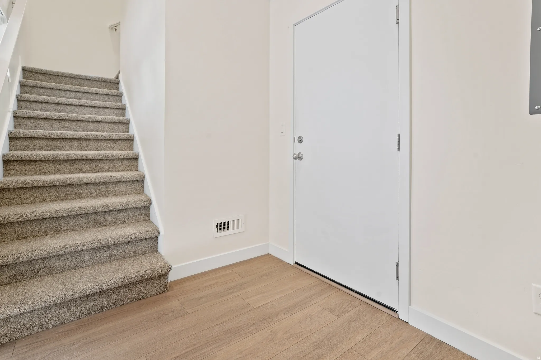 Entryway featuring wood-finish flooring, a white door, and a staircase with neutral-toned carpeting