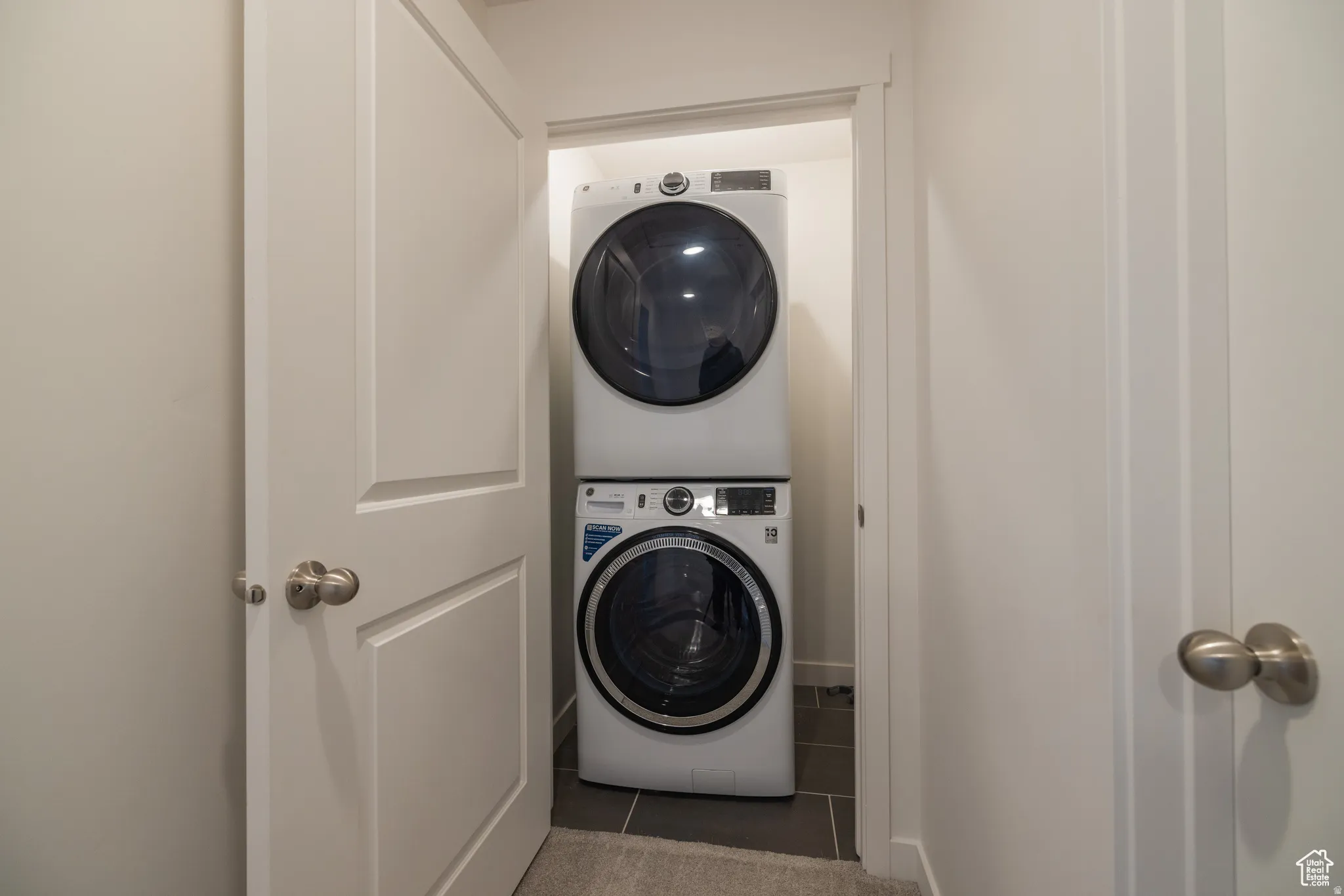 Dedicated laundry closet featuring a stacked washer and dryer, finished with dark tile flooring