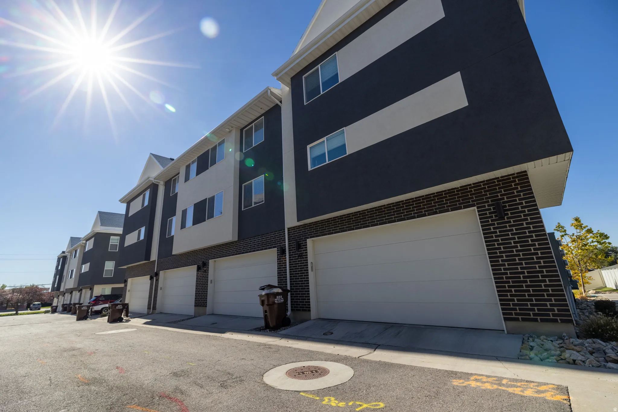Multi-level townhomes featuring two-tone stucco and brick exteriors, white garage doors, and individual entryways