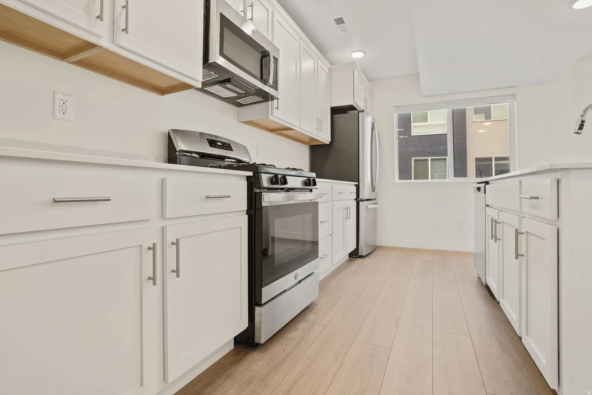 Kitchen featuring white cabinetry, light wood-finish flooring, stainless steel appliances, white countertops, and recessed lighting