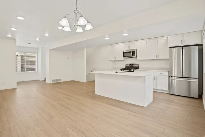 Open-concept kitchen and living area featuring wood-finish flooring, recessed lighting, and a chandelier