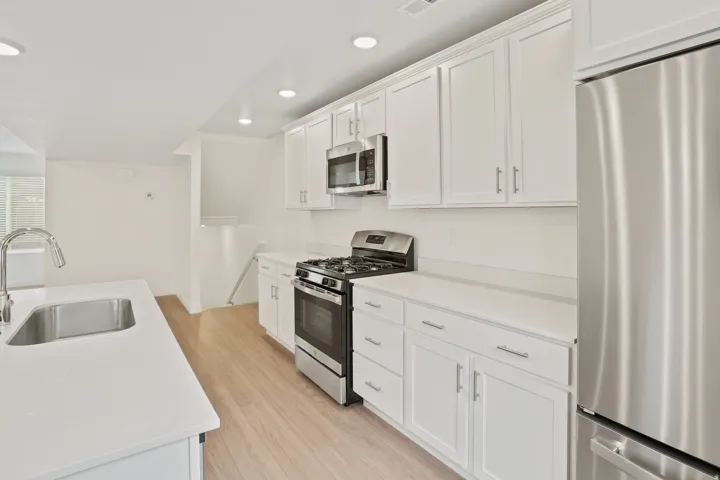 Modern kitchen featuring white shaker cabinetry, stainless steel appliances, light wood-finish flooring, recessed lighting, and white countertops